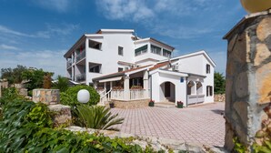 Un edificio bianco di due piani con un balcone, una colonna in pietra e un cortile lastricato.