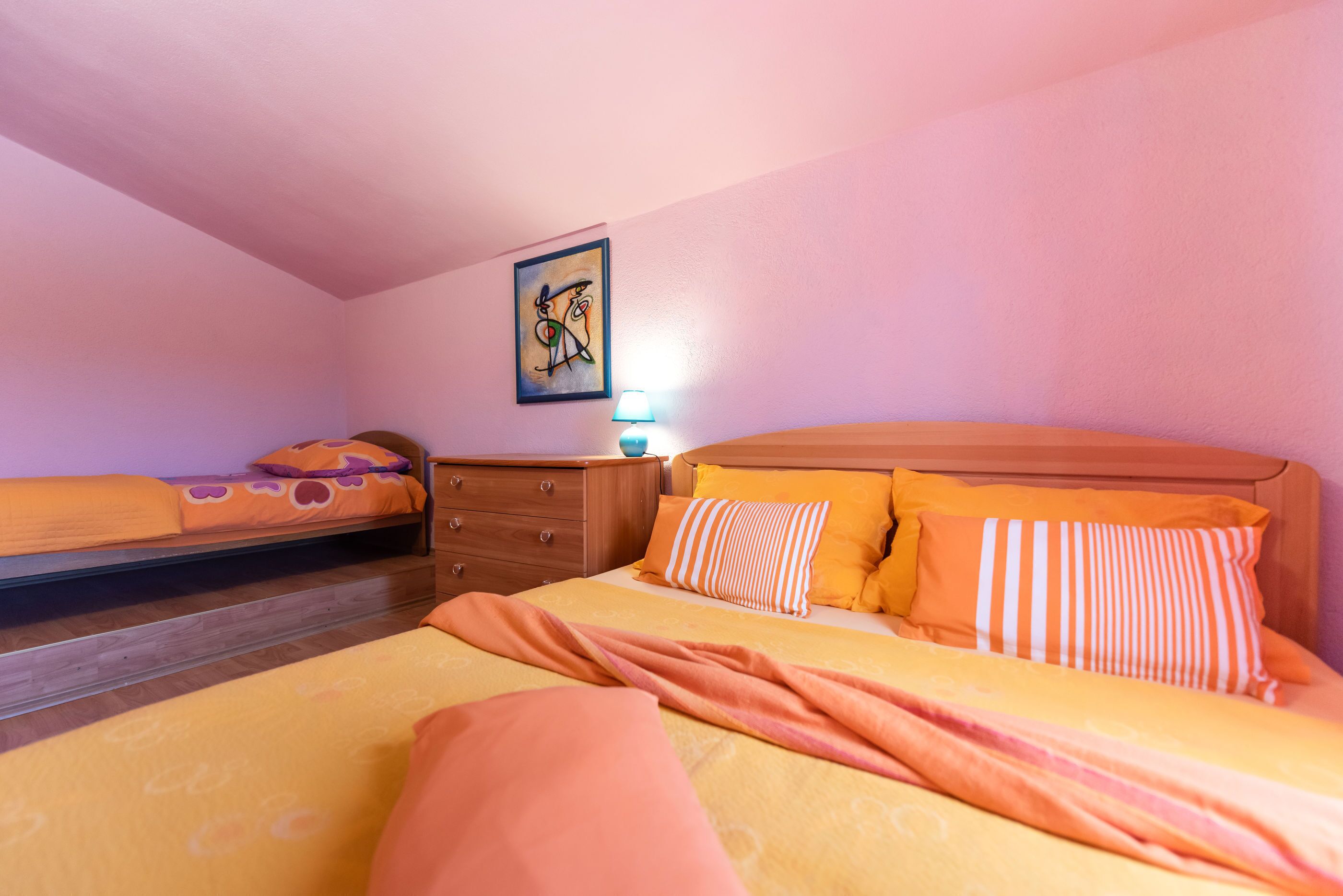 A bedroom with two beds, a wooden headboard, a nightstand, and a wall-mounted artwork.