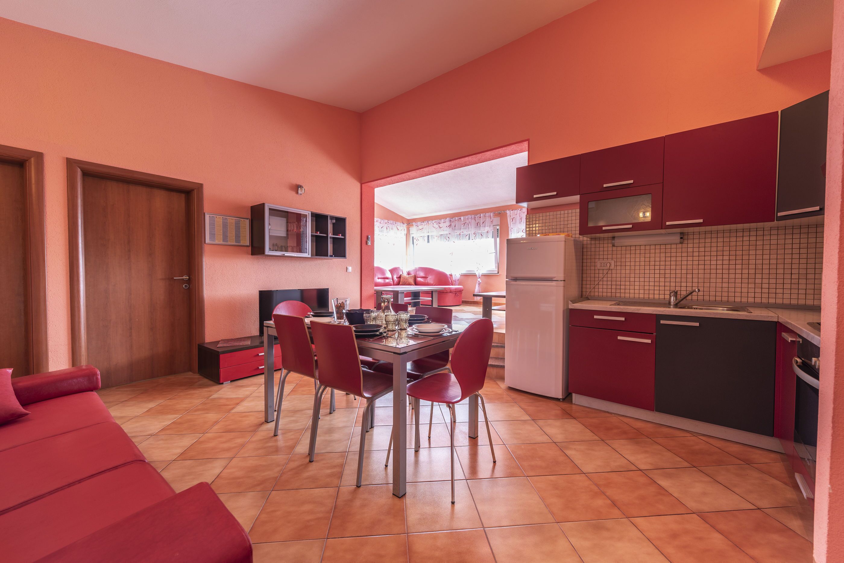 Una cocina compacta con armarios rojos, una mesa de comedor con sillas y un sofá rojo.