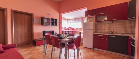 Una cocina compacta con armarios rojos, una mesa de comedor con sillas y un sofá rojo.