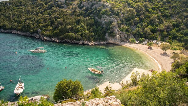 Una zona costiera con barche, una spiaggia e un pendio roccioso.