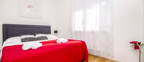 A neatly made bed with a red bedspread, white pillows, and two rolled towels.