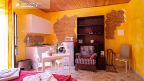 A cozy room with a brick wall, a wooden ceiling, a dining table with chairs, a bookshelf, and a TV. - Patty Studio 'Casa a Chiazzetta' (Castelbuono)