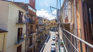 A narrow street with buildings on both sides, balconies with clothes hanging, and a clock tower in the distance. - Patty Studio 'Casa a Chiazzetta' (Castelbuono)