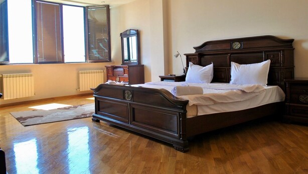 A spacious bedroom with a large bed, wooden headboard, and a view of the city through large windows. - Apartment on Ismayil bay Qurtqashinli 50 (Baku)