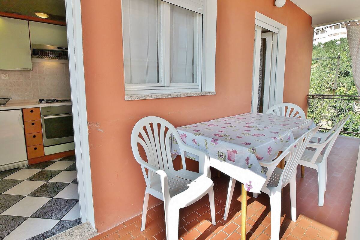 A dining area with a table set for four, white plastic chairs, and a window with white shutters.
