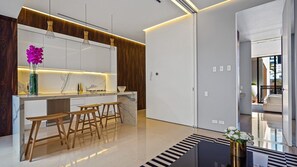 A modern kitchen with a marble countertop, wooden stools, and pendant lighting.
