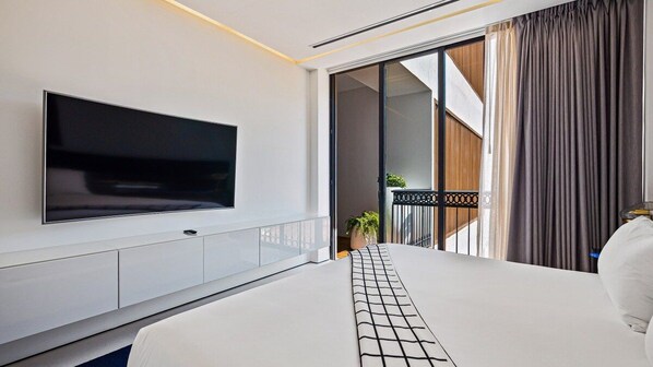 A modern hotel room with a large flat-screen TV mounted on the wall, a bed with a white and black patterned bedspread, and a balcony with a view.