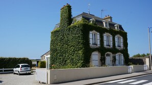 A two-story building with a white facade and a chimney, partially covered in ivy.