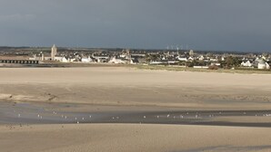 A coastal town with a prominent tower, sandy beach, and wind turbines in the distance.
