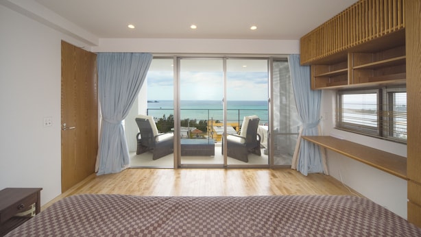 A bedroom with a large bed, a balcony with a view of the sea, and a wooden shelf. - Onnason vacation rental K (Onna)