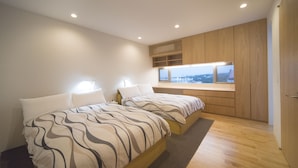A modern bedroom with two beds, a window with a city view, wooden cabinetry, and recessed ceiling lights. - Onnason vacation rental K (Onna)