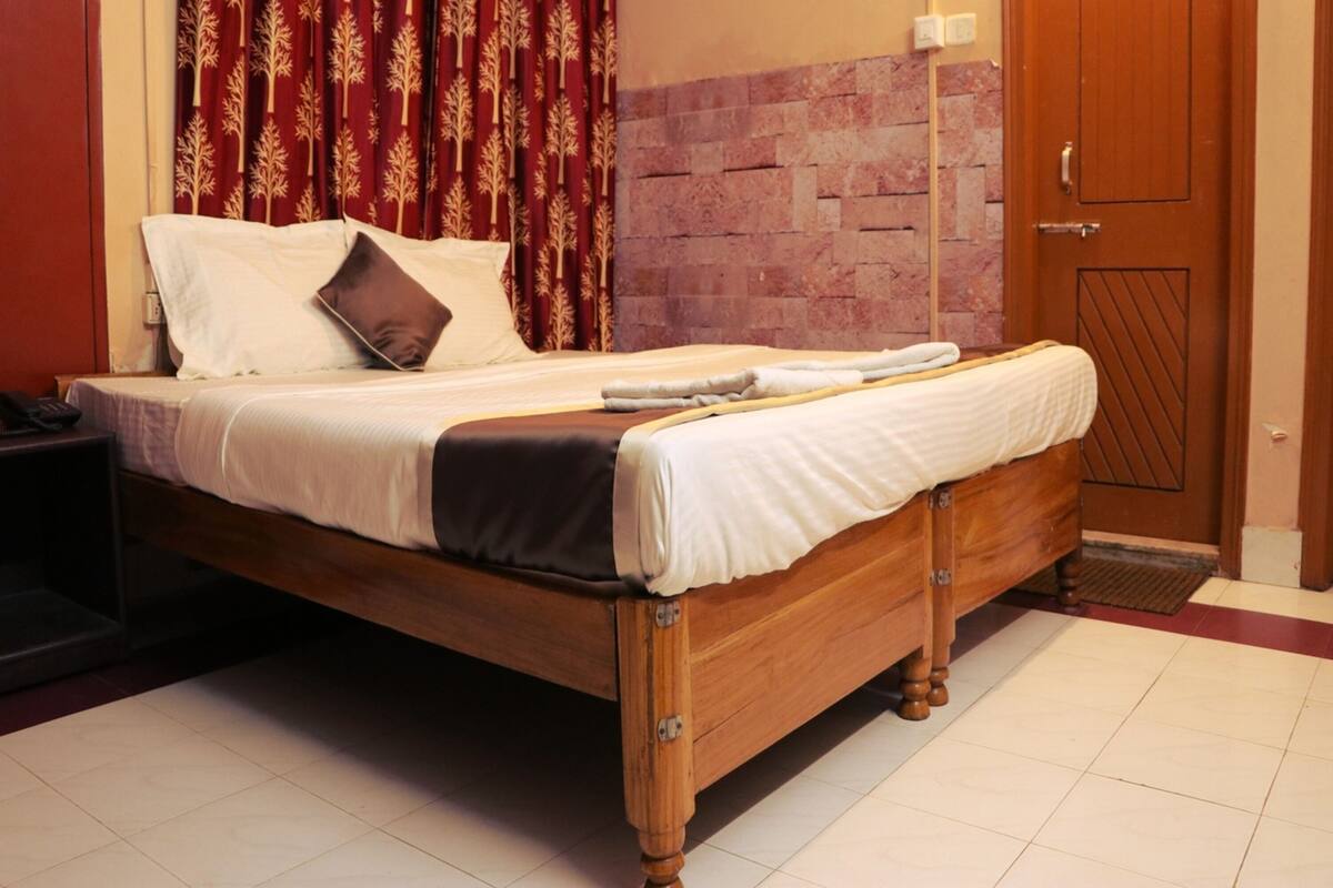 A wooden bed with a white and brown bedspread, a bedside table, and a red curtain with a leaf pattern.