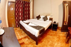 A hotel room with a bed, a nightstand, a mirror, and a wardrobe. - Om Shree Cottage (Guwahati)