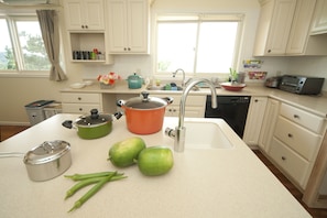 A kitchen with white cabinets, a sink, a stove, and a microwave. There are green vegetables on the counter.