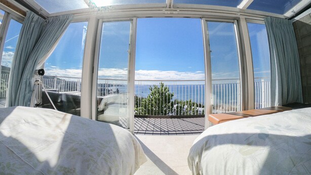 A room with a large glass ceiling, two beds, a small table, and a view of the sea. - Onnason vacation rental C (Onna)
