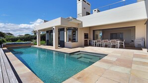 A modern outdoor pool area with a clear blue pool, a wooden deck, and a patio with outdoor furniture. - Vacation Villa 2WW (Cape Town)