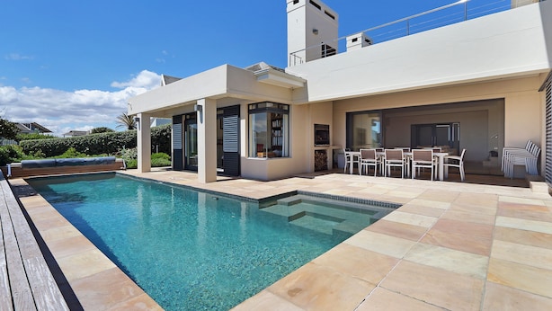 A modern outdoor pool area with a clear blue pool, a wooden deck, and a patio with outdoor furniture. - Vacation Villa 2WW (Cape Town)