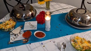 Una mesa vestida con mantel azul, una vela, un florero con girasoles y diferentes platos, incluyendo una ensalada y un bol de sopa.