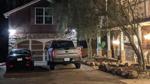 Un estacionamiento con dos vehículos estacionados, un edificio de fachada de piedra y un árbol en primer plano.