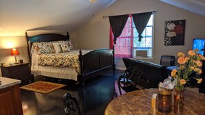 Un dormitorio con cama, escritorio, silla, mesa redonda, ventana con cortinas, ventilador de techo y aire acondicionado de pared.