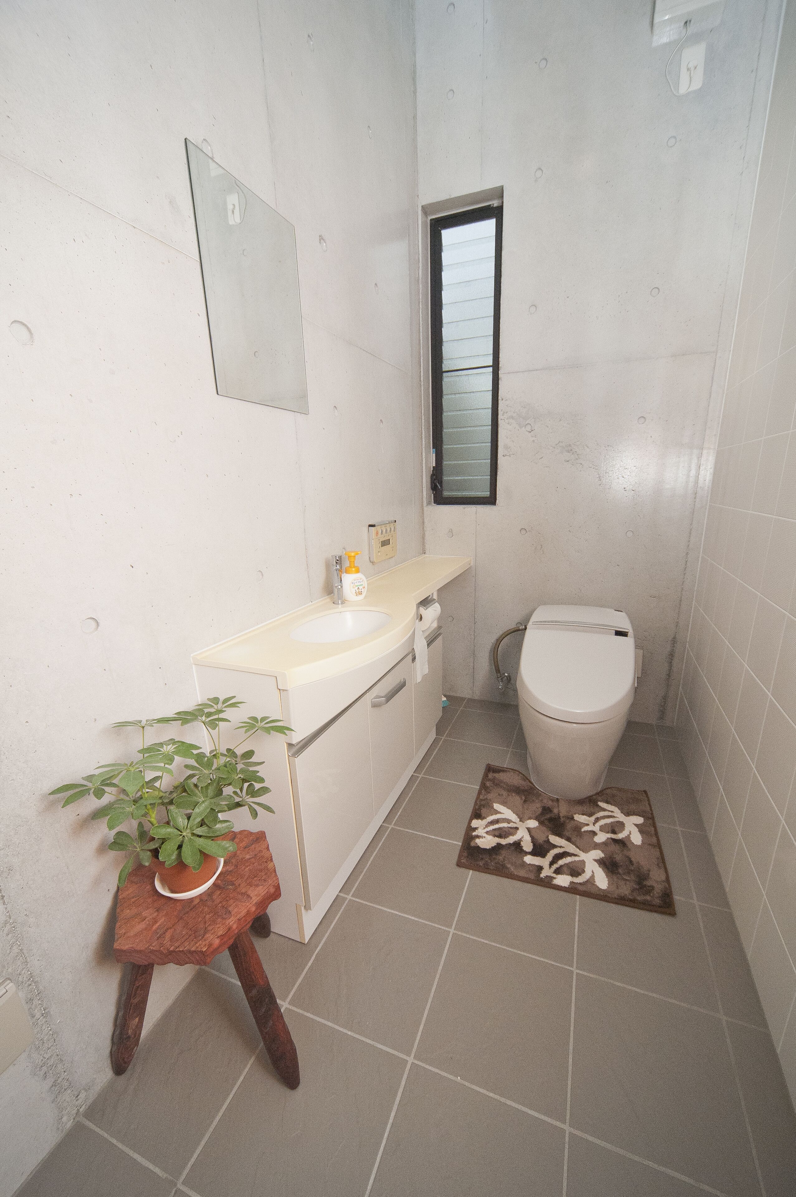 Une petite salle de bain avec des toilettes, un lavabo et une plante en pot posée sur un tabouret en bois.