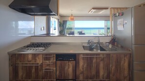 Une cuisine équipée d’une cuisinière à gaz, d’un lave-vaisselle et d’une grande fenêtre donnant sur l’océan.
