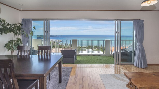 Un balcon spacieux avec vue sur l’océan, un coin repas avec une table et des chaises, et une table basse en bois.