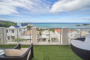 A balcony with a view of the sea, a grassy area, and wicker furniture. - Onnason vacation rental  J (Onna)