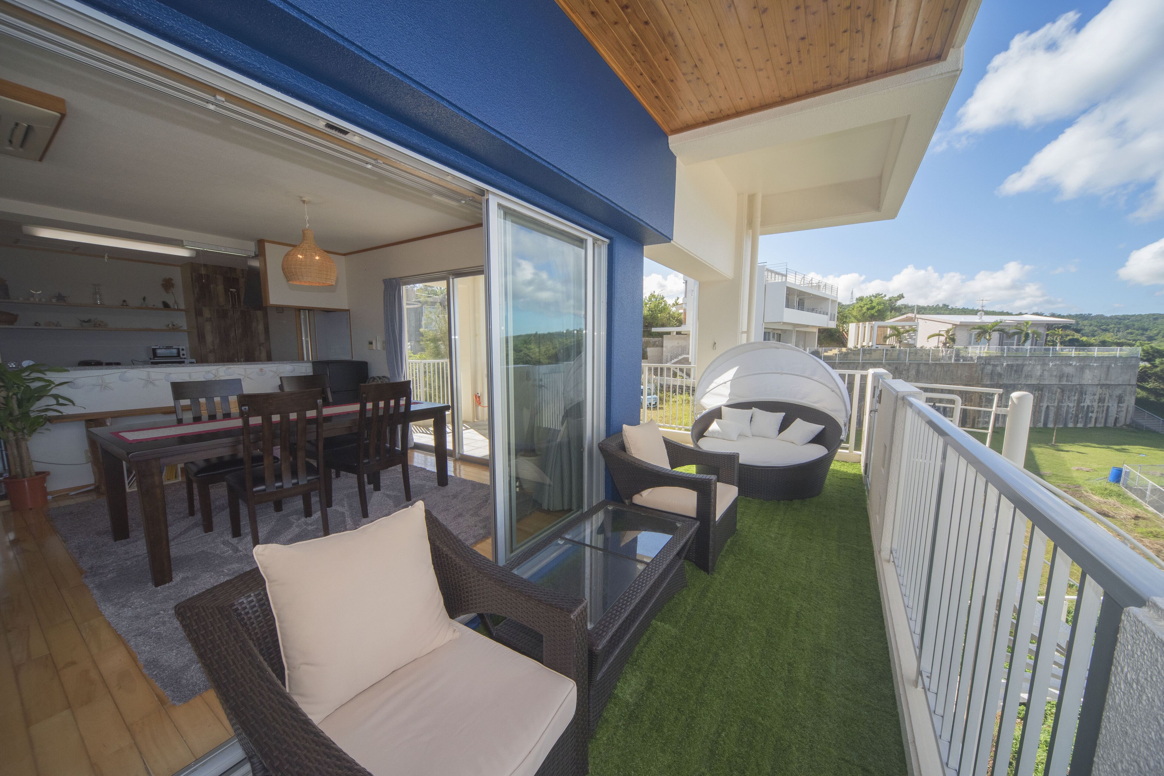 A balcony with a glass table, wicker chairs, and a white sofa.