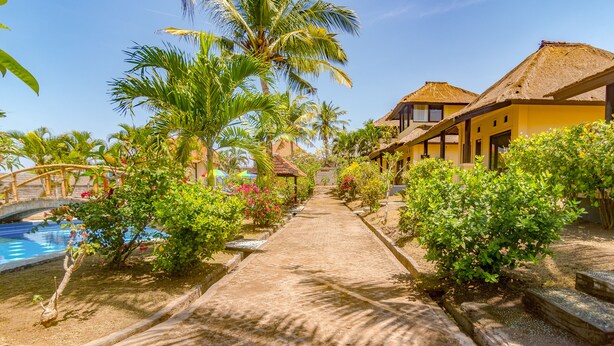 A pathway leading to a pool area with palm trees and a thatched-roof building. - Villa Sari Cucukan (Gianyar)