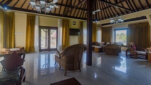 A spacious living area with a high ceiling, wicker furniture, and a large window providing natural light. - Villa Sari Cucukan (Gianyar)