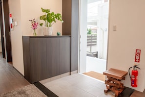 Un hall d’hôtel moderne avec un comptoir d’accueil en bois foncé, une plante en pot et un extincteur fixé au mur.