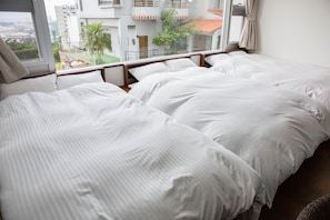 Une chambre d’hôtel avec deux lits, une grande fenêtre donnant sur des immeubles et des palmiers, et un balcon.