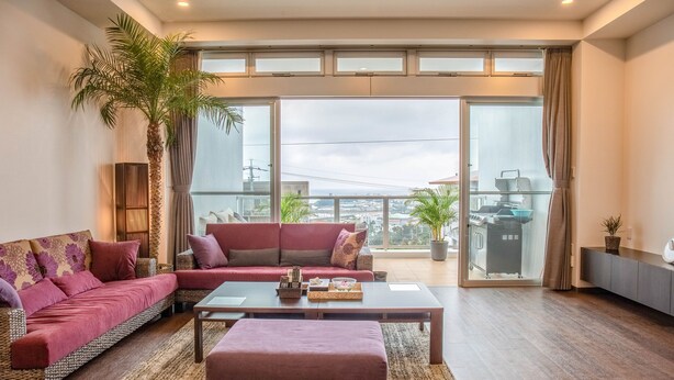 A spacious living room with a large sofa, a coffee table, and a view of the city through large windows. - Onnason vacation rental N (Onna)