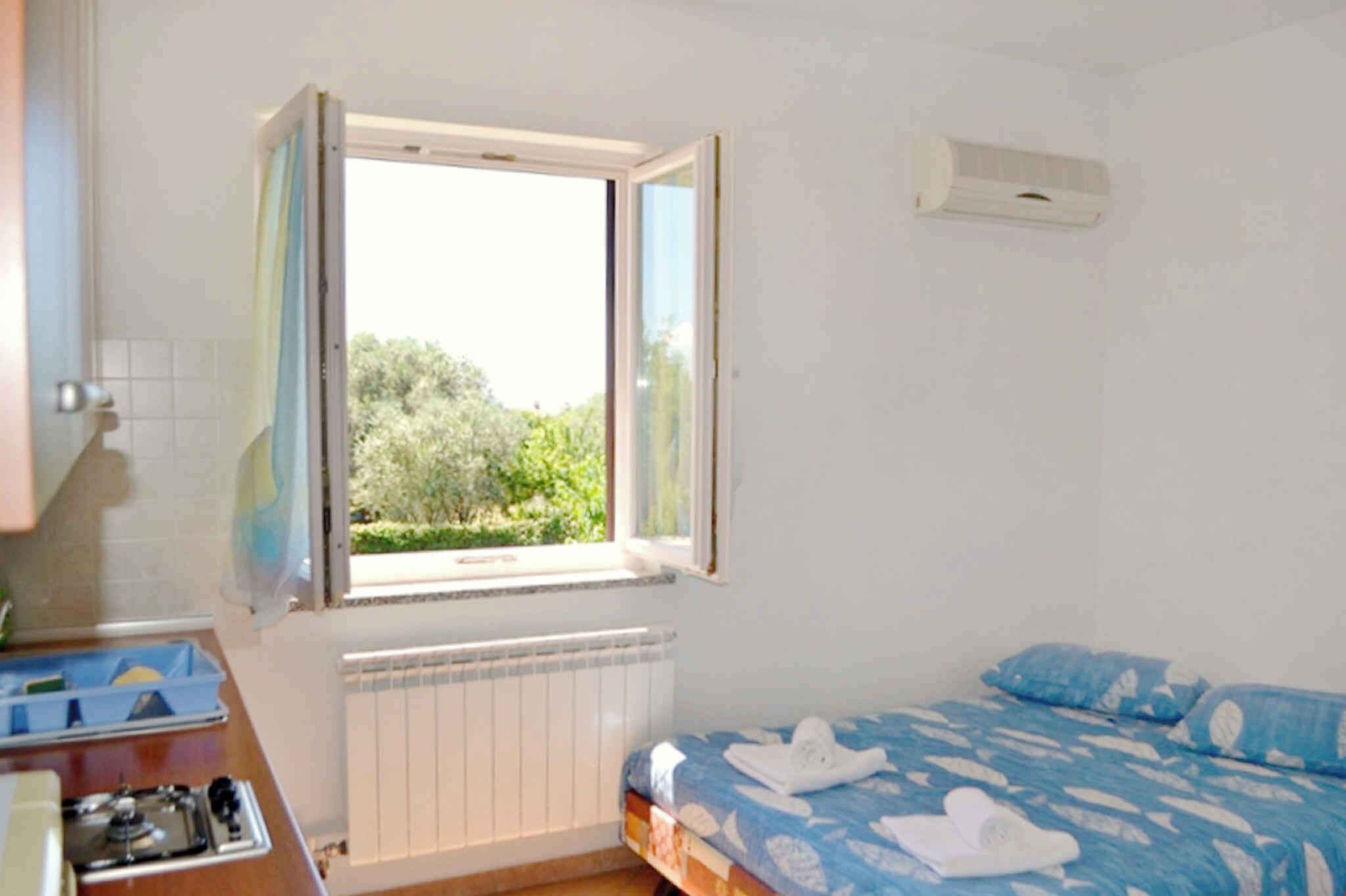 Een slaapkamer met een bed, een raam met gordijnen, een radiator en een klein tafeltje met een gasfornuis.