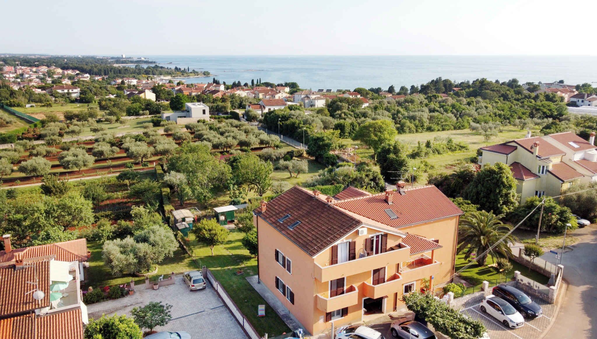 A two-story building with a flat roof, surrounded by greenery and a view of the sea.
