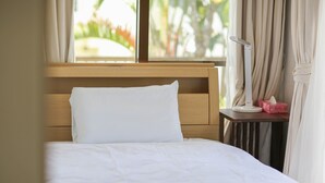 Un lit bien fait, avec du linge de lit blanc, une tête de lit en bois et une table de chevet sur laquelle se trouvent une lampe et une boîte de mouchoirs.
