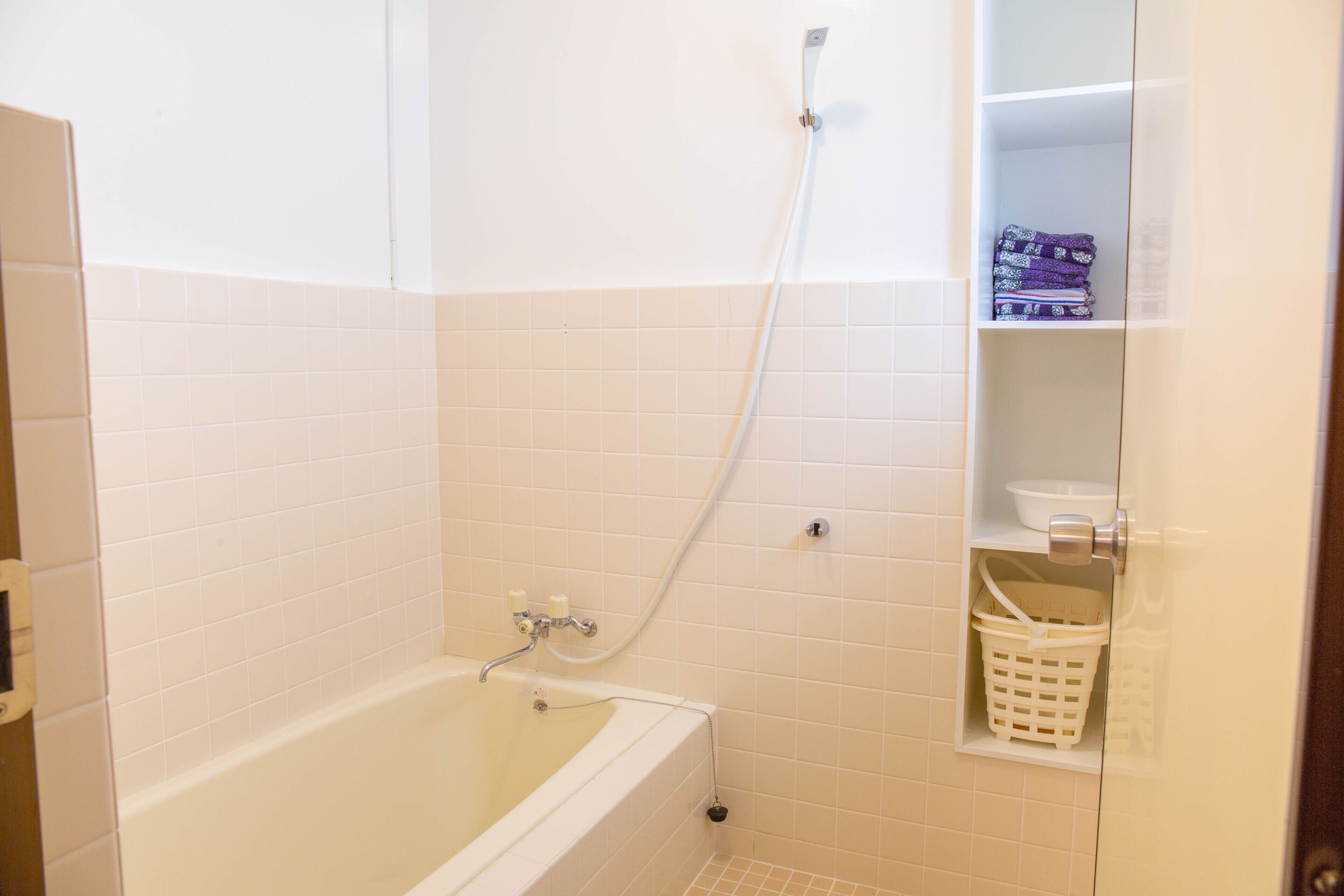 Une salle de bain avec une baignoire, une douche et une étagère sur laquelle se trouvent un panier et un bol.