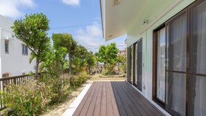Une terrasse en bois avec une balustrade blanche, menant à un bâtiment doté de grandes fenêtres et d’une façade verte.