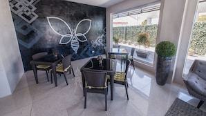 Un comedor moderno con una mesa de vidrio y sillas de mimbre, una pared decorativa grande con patrones geométricos y vistas al exterior a través de amplios ventanales.