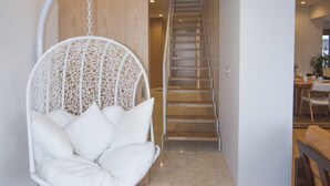 Een modern interieur met een houten trap, een witte hangstoel en een eethoek.