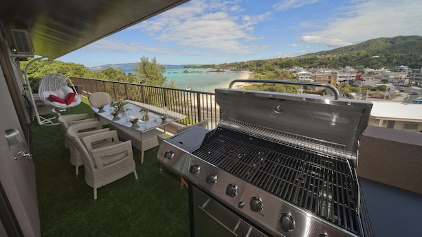 Een balkon met een barbecue, rieten stoelen en een tafel met een vaas.