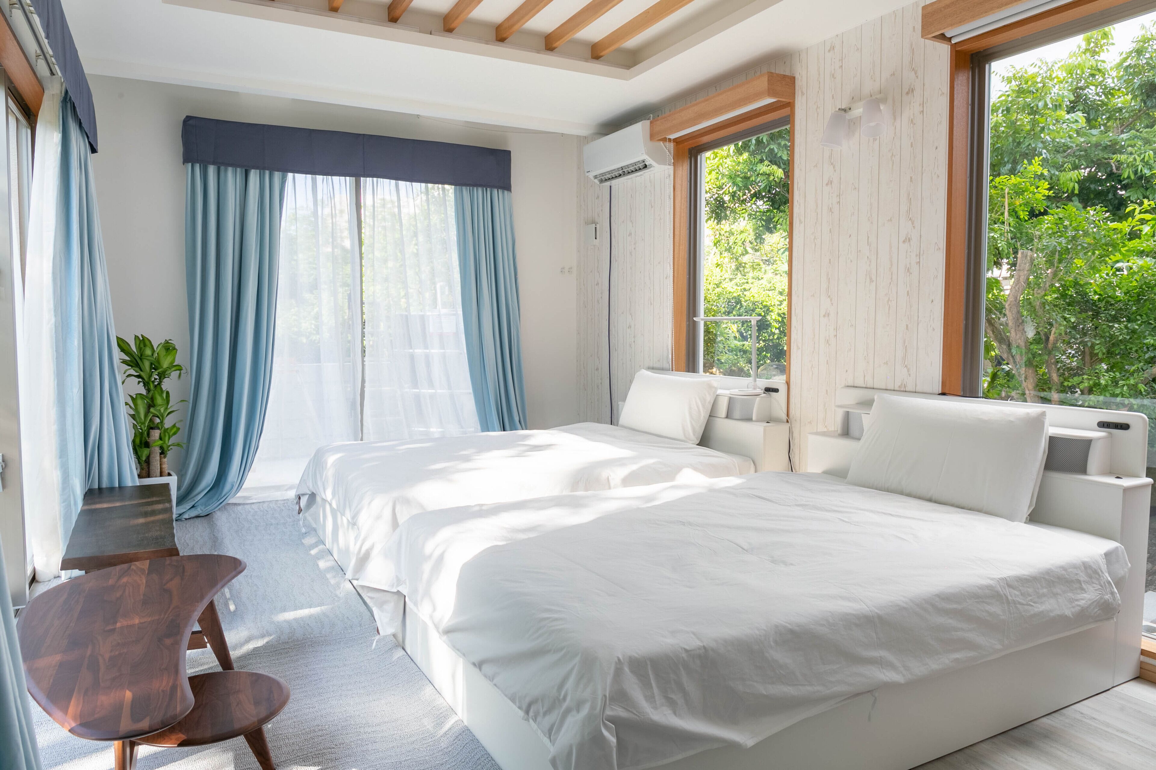 Quarto moderno com duas camas, teto de madeira e uma janela grande com cortinas.