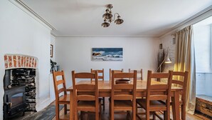A dining area with a wooden table and chairs, a stone fireplace, and a painting on the wall. - A beautiful harbourside four-bedroom cottage with harbour views (Boscastle)