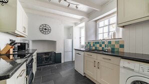 A modern kitchen with a black countertop, white cabinets, a clock, and a washing machine. - A beautiful harbourside four-bedroom cottage with harbour views (Boscastle)