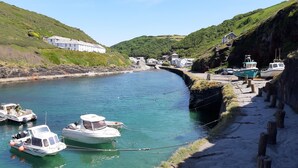 A coastal village with boats docked along a narrow waterway, surrounded by lush green hills and traditional white buildings. - A beautiful harbourside four-bedroom cottage with harbour views (Boscastle)