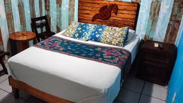A bed with a floral bedspread, a wooden headboard with a horse decoration, a small round table, and two chairs.