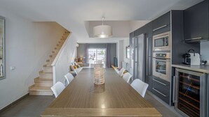 Een moderne keuken met een houten eettafel, grijze kastjes en roestvrijstalen apparatuur.
