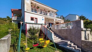 Una casa de dos pisos amb un balcó, un cadireta i una paret de pedra.